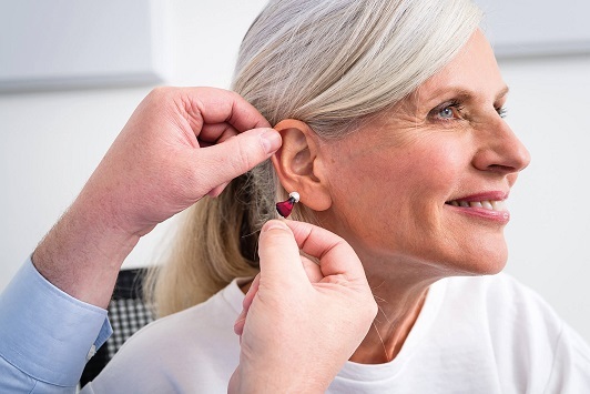 Ältere Frau bekommt ein modernes Hörgerät angepasst, Hörakustiker berät einfühlsam.